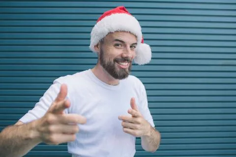 Positive guy with santa hat is looking on camera and smiling. He is pointing  Fotos Stock