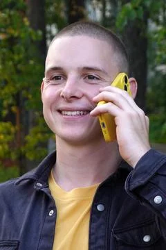 Positive guy is smiling and talking on a yellow cell phone outside. wireless Foto stock