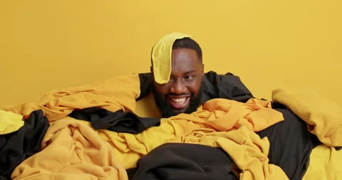 Positive handsome bearded man with dark skin poses near pile of clothes has sock Stock Footage 156632728