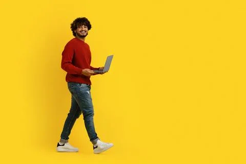 Positive hindu guy using laptop and walking towards copy space Stock Photos