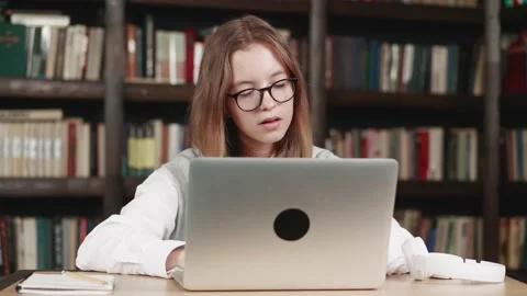 Positive kid in glasses and using laptop at home library studying online. Side Stock Footage 160112931