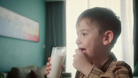 Positive kid smiling while having breakfast at home. Cute boy drinking milk and Stock Footage 317776152