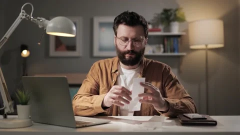Positive man enters data from pay check into computer. Beard freelancer in home Stock-Footage 188733537