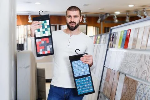 Positive man holding sample of kitchen ceramic tile in modern store Stock Photos