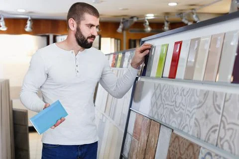 Positive man holding sample of kitchen ceramic tile in modern store Stock Photos