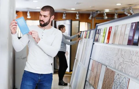 Positive man holding sample of kitchen ceramic tile in modern store Stock Photos
