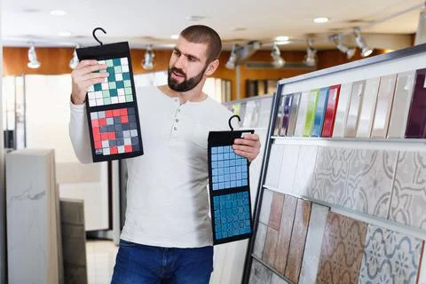 Positive man holding sample of kitchen ceramic tile in modern store Stock Photos