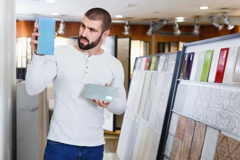 Positive man holding sample of kitchen ceramic tile in modern store Stock Photos