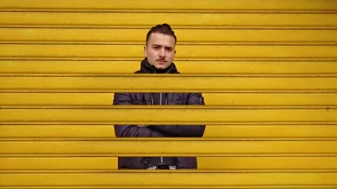 Positive man in jacket stuck in yellow texture of shutters Stock Footage 145643574