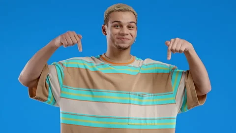 Positive man pointing down to advertising area. Blue background. Young teenager Stock Footage 222986765