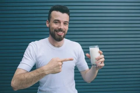 Positive man is standing and posing. He is holding glass of milk and pointing Stockfoto's