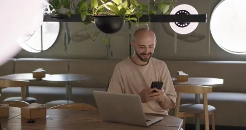 Positive man using laptop and cell phone at cafe table Stock Footage 159083451