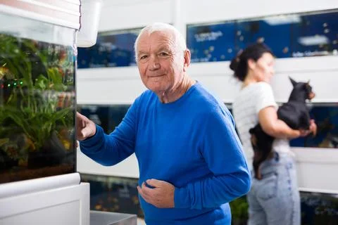 Positive mature man chooses aquarium fish in pet shop Stock Photos