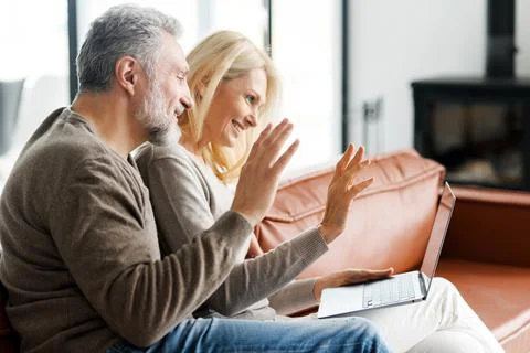 Positive middle-aged couple is using laptop for video call Stock Photos