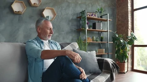 Positive middle aged man sit divan furniture enjoy room in house 動画素材 166624034
