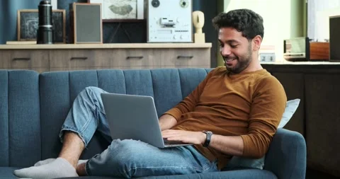 Positive Middle Eastern Man Typing on Laptop While Seated on a Sofa Stock Footage 254440631