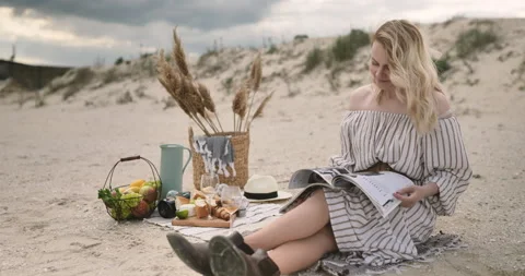 Positive model sitting on plaid on the Ocean seaside, eating fruits and read mag Stock Footage 155155851