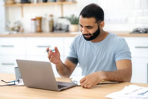 Positive modern Indian man, freelancer, designer or student, sitting at a Stock Photos