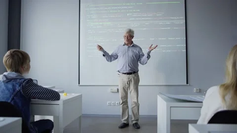 Positive old teacher explaining computer science to children showing balance Stock Footage 142492841