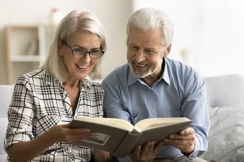 Positive older husband and wife watching pictures in photo album Stock Photos