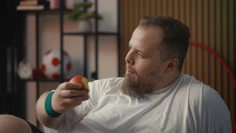 Positive plus-size man eating fresh apple after exercise, self-improvement goal Vídeos de archivo 310003118