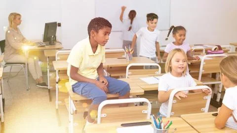 Positive primary school students are talking about homework at desk Stock Photos