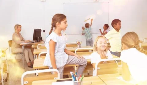 Positive primary school students are talking about homework at desk Stock Photos