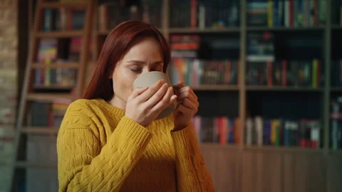 Positive red-haired female student enjoying warm tea during bookshop study break Stock Footage 340267276