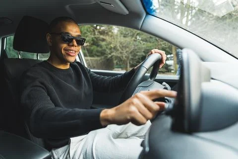Positive smiling casually dressed young adult guy sitting on driver's seat and Stock Photos