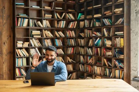 Positive smiling Indian freelancer guy using laptop for virtual meeting at Stock Photos