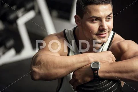 Positive well built man leaning on a dumbbell Stock Photos