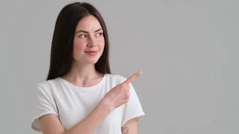 A positive woman wearing basic T-shirt is pointing to the side  Video stock 154947401