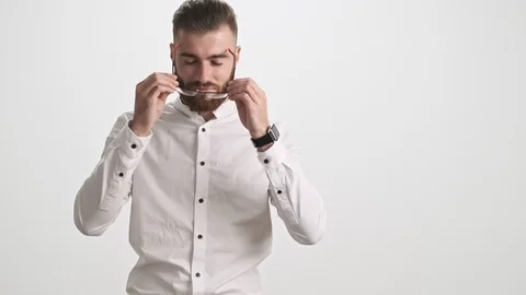 A positive young bearded man puts on glasses over white background Stock Footage 125321017