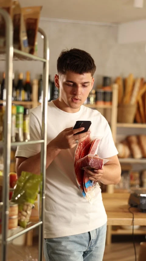 Positive young guy purchaser scanning with smartphone QR code of dried sausage Stock Footage 313096814
