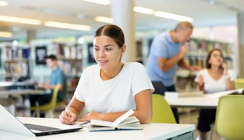 Positive young lady working remotely using a computer in a quiet library Foto stock