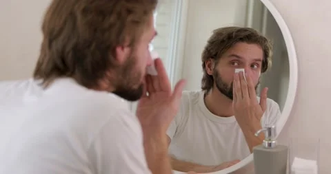 Positive young man with beard using cotton pad and cleansing lotion for face Stock Footage 142528484