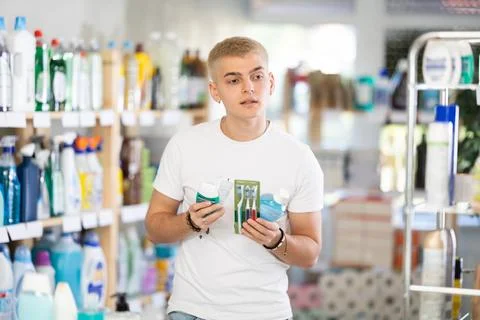 Positive young man choosing toothpaste and toothbrush, dental kit in store Фото