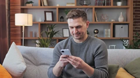 Positive young man using smartphone indoors texting messages at home office. Video stock 172393054