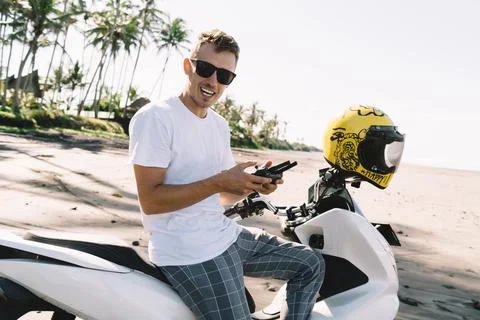 Positive young man using UAV controller while sitting on motorcycle against Stock Photos