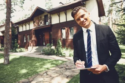 Positive young realtor making notes while standing in front of the house Stock Photos