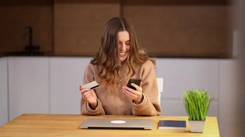 A positive young woman pays for online purchases with her smartphone and bank Stock Footage