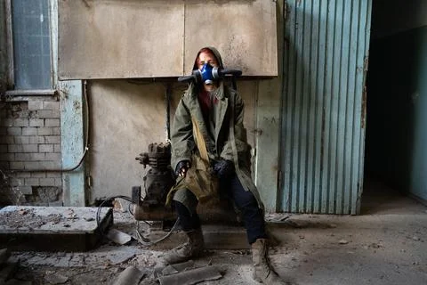 Post apocalyptic female survivor in gas mask sitting in a ruined building. En Stock Photos