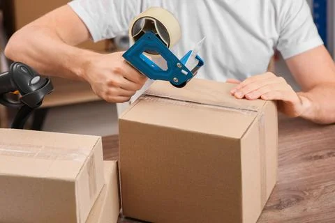 Post office worker packing parcel at counter indoors, closeup Photos