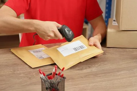 Post office worker with scanner reading parcel barcode at counter, closeup Photos