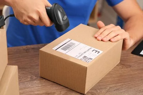 Post office worker with scanner reading parcel barcode at counter, closeup Foto stock