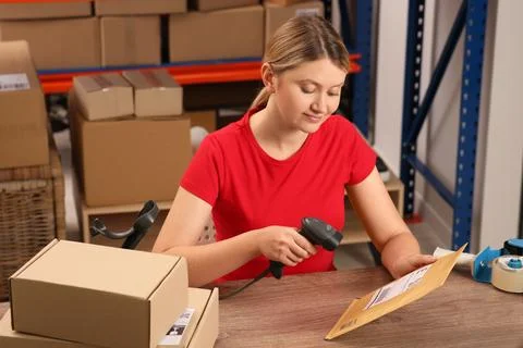 Post office worker with scanner reading parcel barcode at counter indoors Photos
