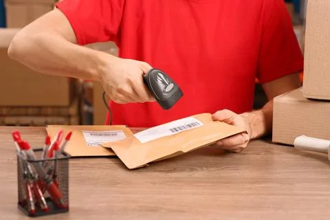 Post office worker with scanner reading parcel barcode at counter, closeup Stock Photos
