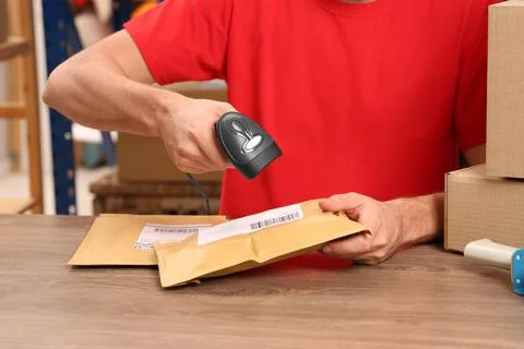 Post office worker with scanner reading parcel barcode at counter, closeup Foto stock