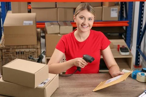 Post office worker with scanner reading parcel barcode at counter indoors Foto stock