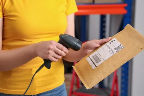 Post office worker with scanner reading parcel barcode indoors, closeup Photos